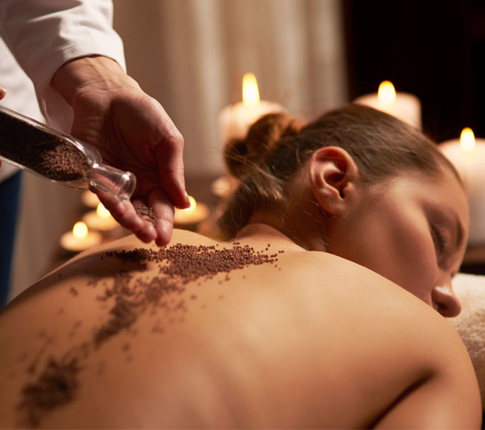A woman getting a full body coffee scrub in a spa by a professional therapist