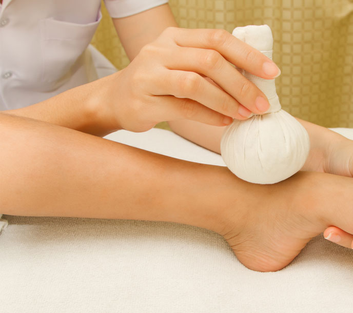 A lady getting a relaxing pain relieving foot massage in a spa with potli herbal ball compress