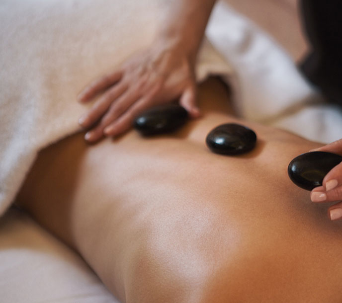 A lady with heated volcanic stones on the back getting a professional hot stone therapy at a spa by skilled therapist